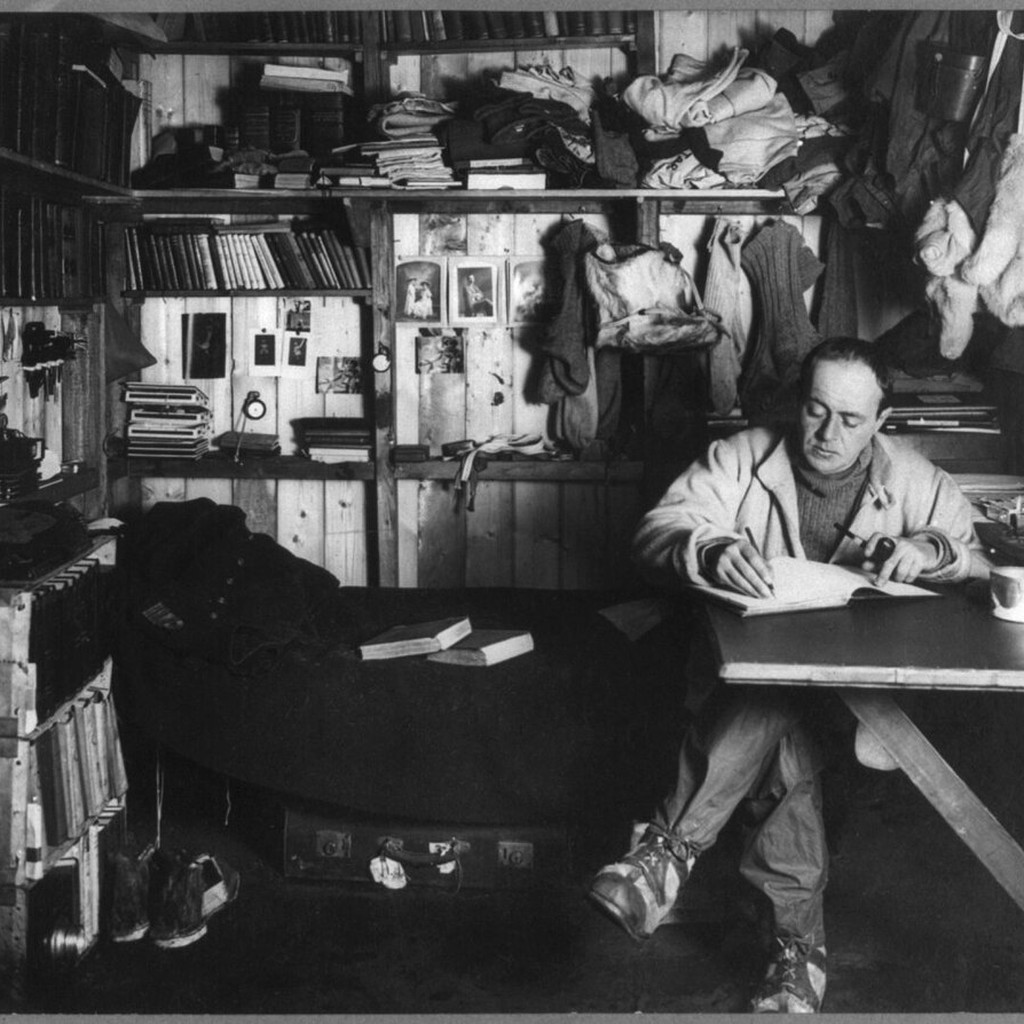 テラ・ノヴァ遠征の冬営舎で机に向かい、日記を書くロバート・ファルコン・スコット。Herbert Ponting撮影。